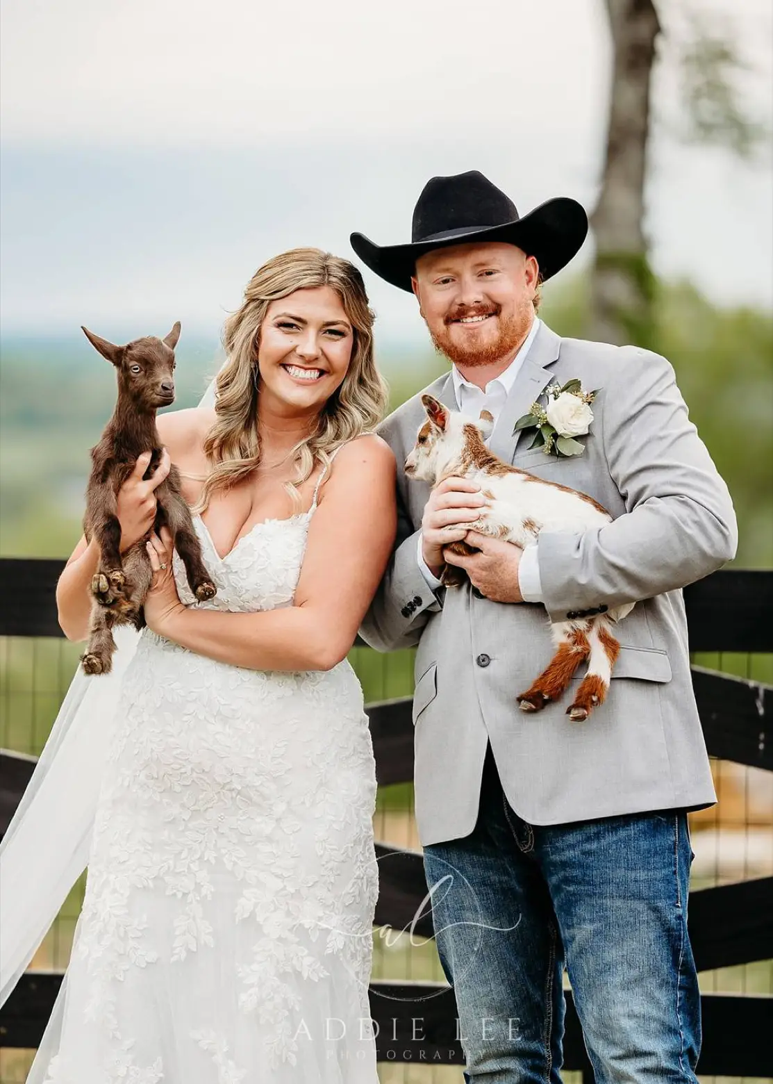 A newlywed couple smile at a fence, each cradling a baby goat during a guided animal moment at LIKAZOO.