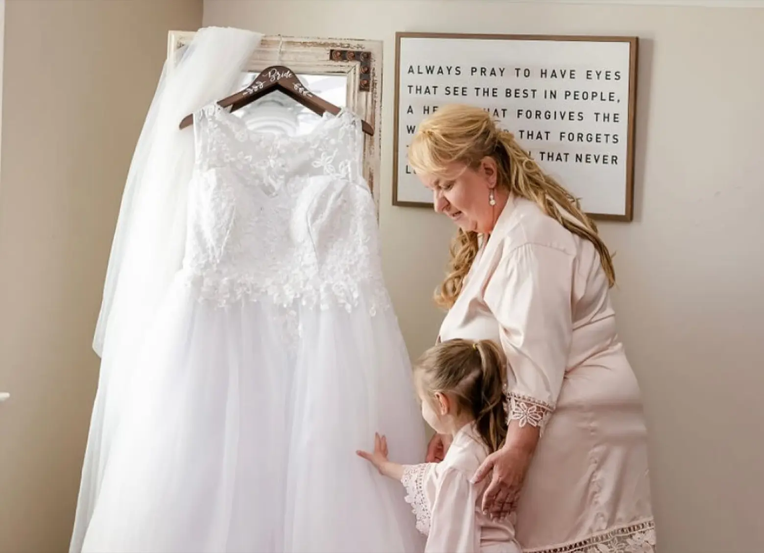 A wedding dress on a hanger by a bright window as a family member helps get ready in the suite.