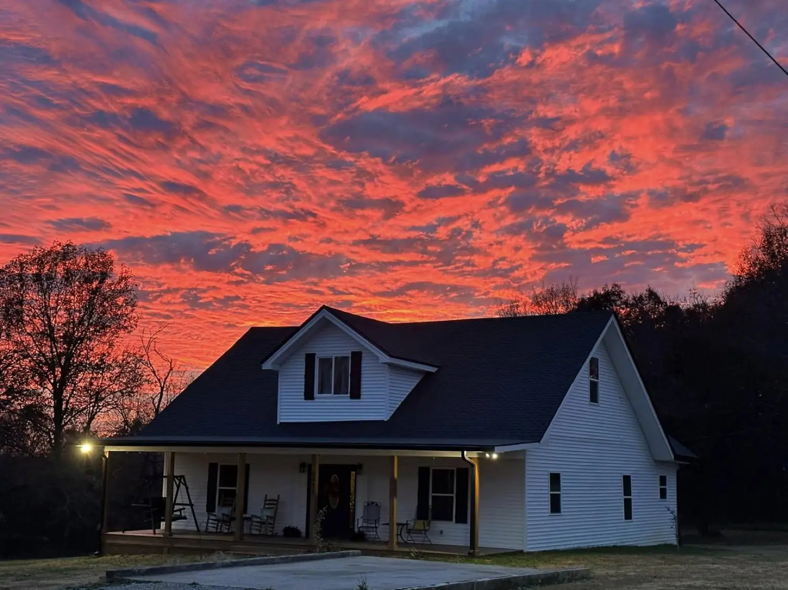 An on-site lodging farmhouse at LIKAZOO at dusk — a white wraparound-porch home glowing under a vivid pink-and-orange Tennessee sunset.