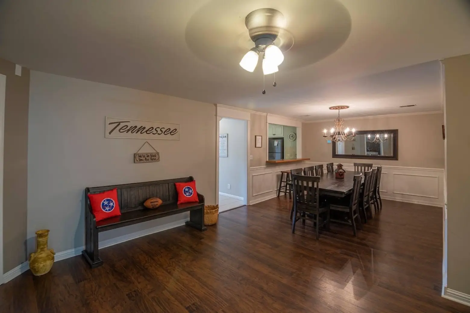 A large farmhouse dining room at LIKAZOO with a long wooden table set for a big group, a chandelier, and a Tennessee wall sign.