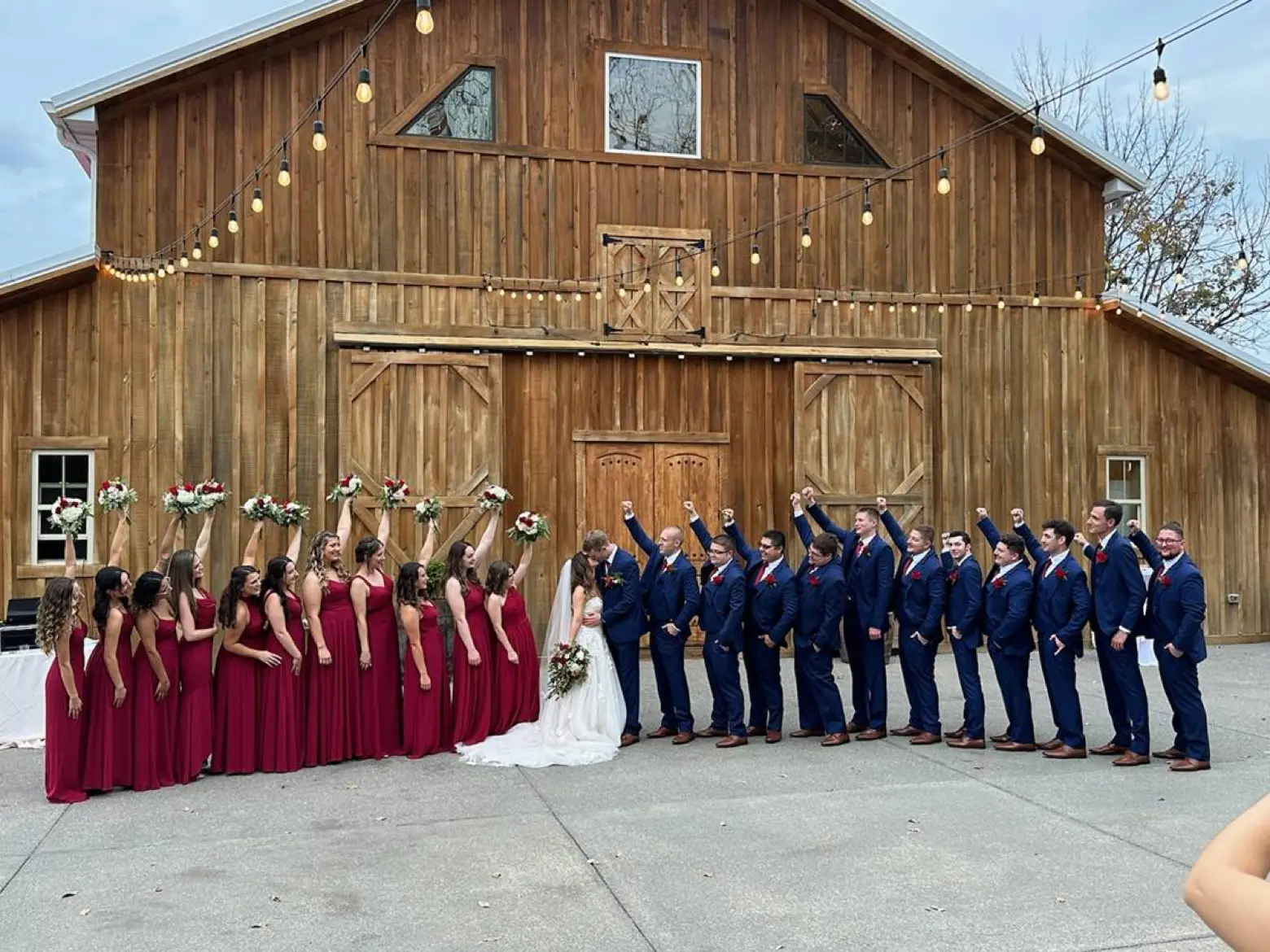 The full wedding party lined up across the lawn in front of the white barn.